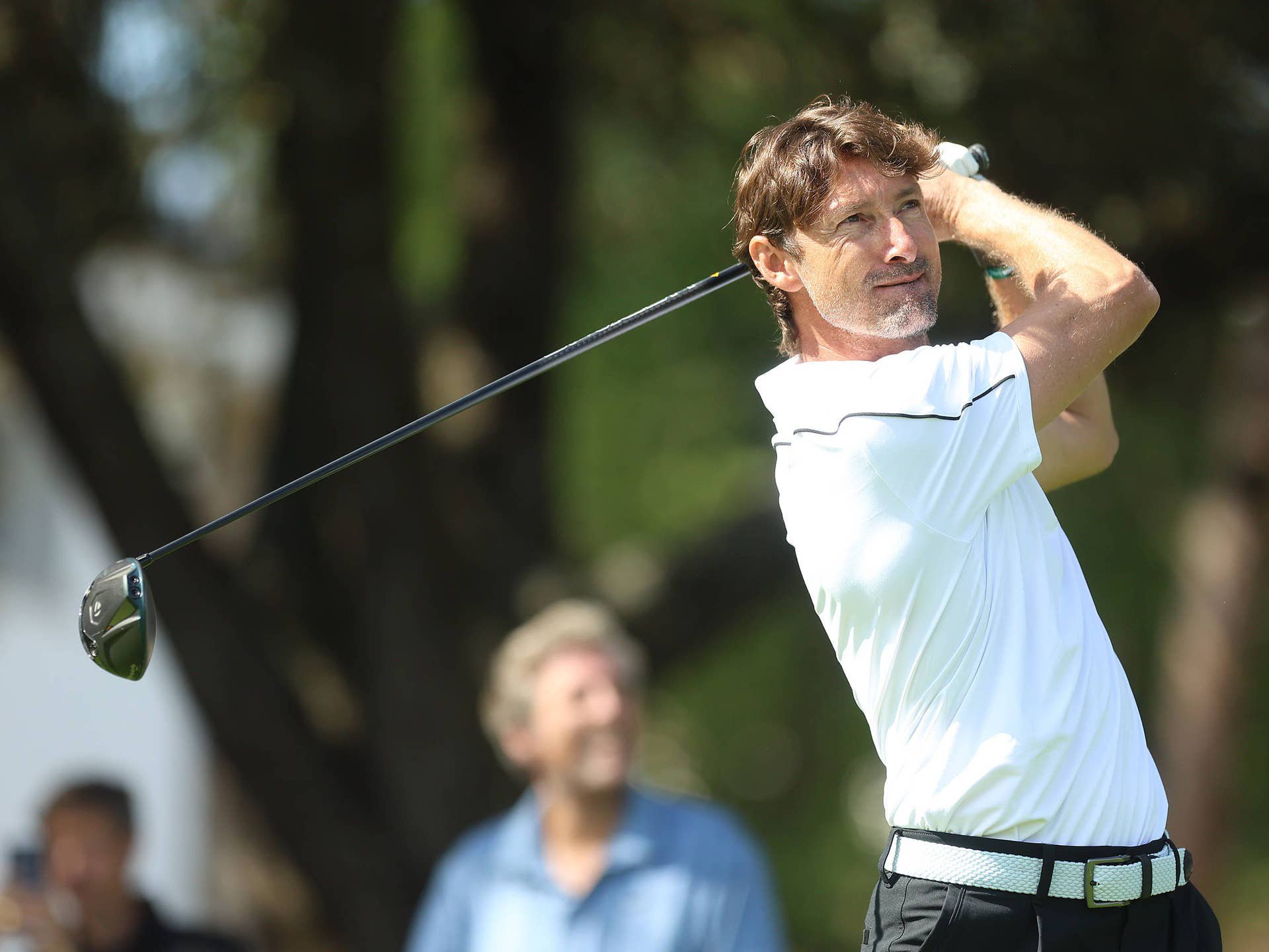 Mann im weißen Polohemd schwingt einen Golfschläger auf einem Golfplatz im Freien.