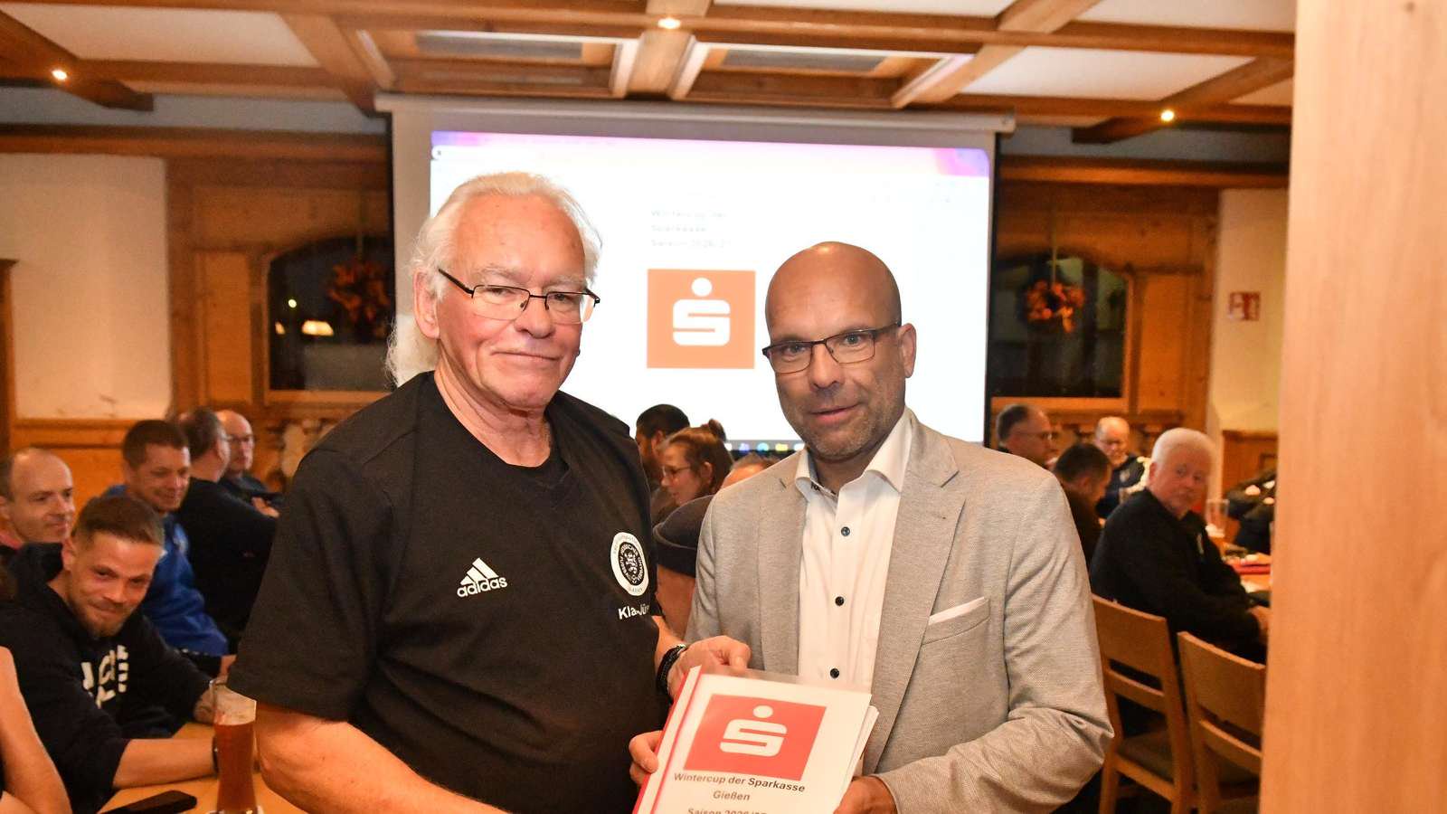 Michael Weber (r.), Filialleiter der Sparkasse Gießen in Linden, überreicht Kreisjugendfußballwart und Klassenleiter der Wintercup-Hallenrunde Klaus-Jürgen Schretzlmaier die erneuten Förderungsunterlagen.