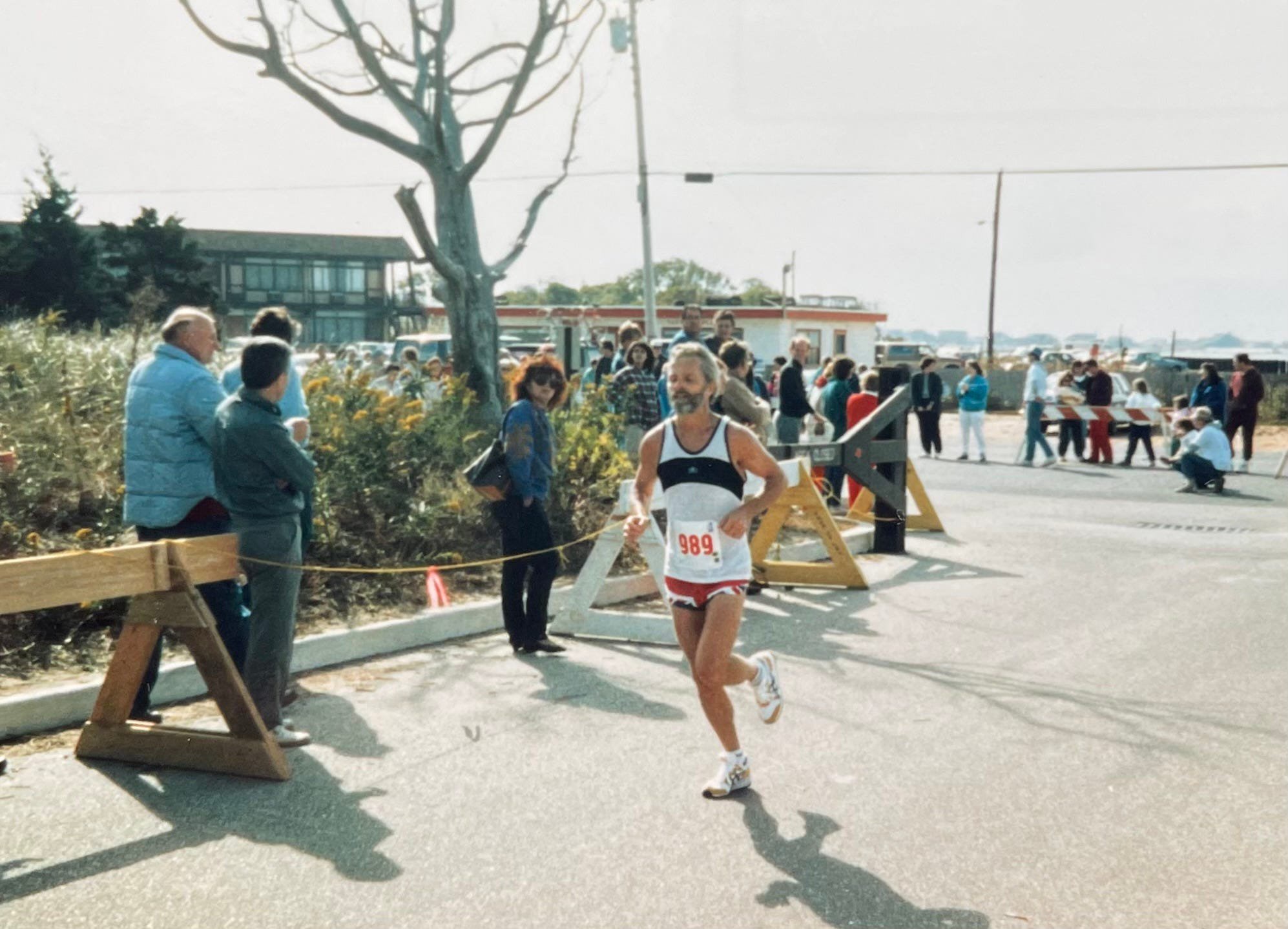 A runner wearing number 989 participates in a road race with spectators in the background.