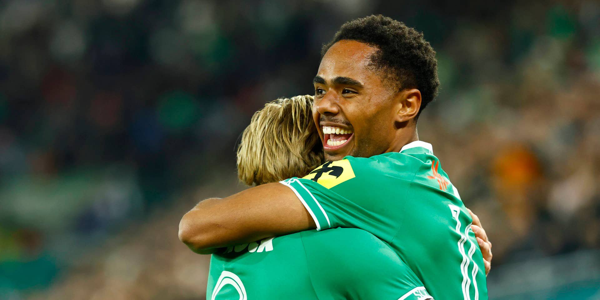 Zwei Rapid Wien-Spieler umarmen sich jubelnd nach einem Tor im Stadion.