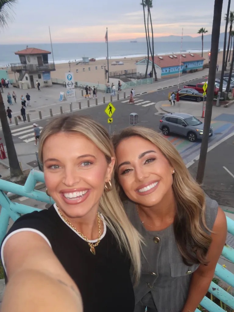 Two women taking a selfie on a balcony overlooking a beach.