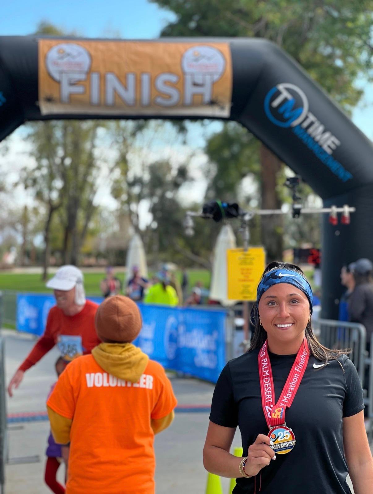 Julianna Mangano, 26, poses for a photo beneath a finish line archway wearing a marathon finisher medal.