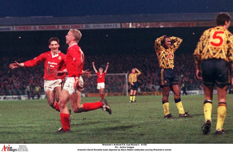 Arsenal’s David Rocastle looks dejected as Steve Watkin celebrates scoring Wrexham’s winner