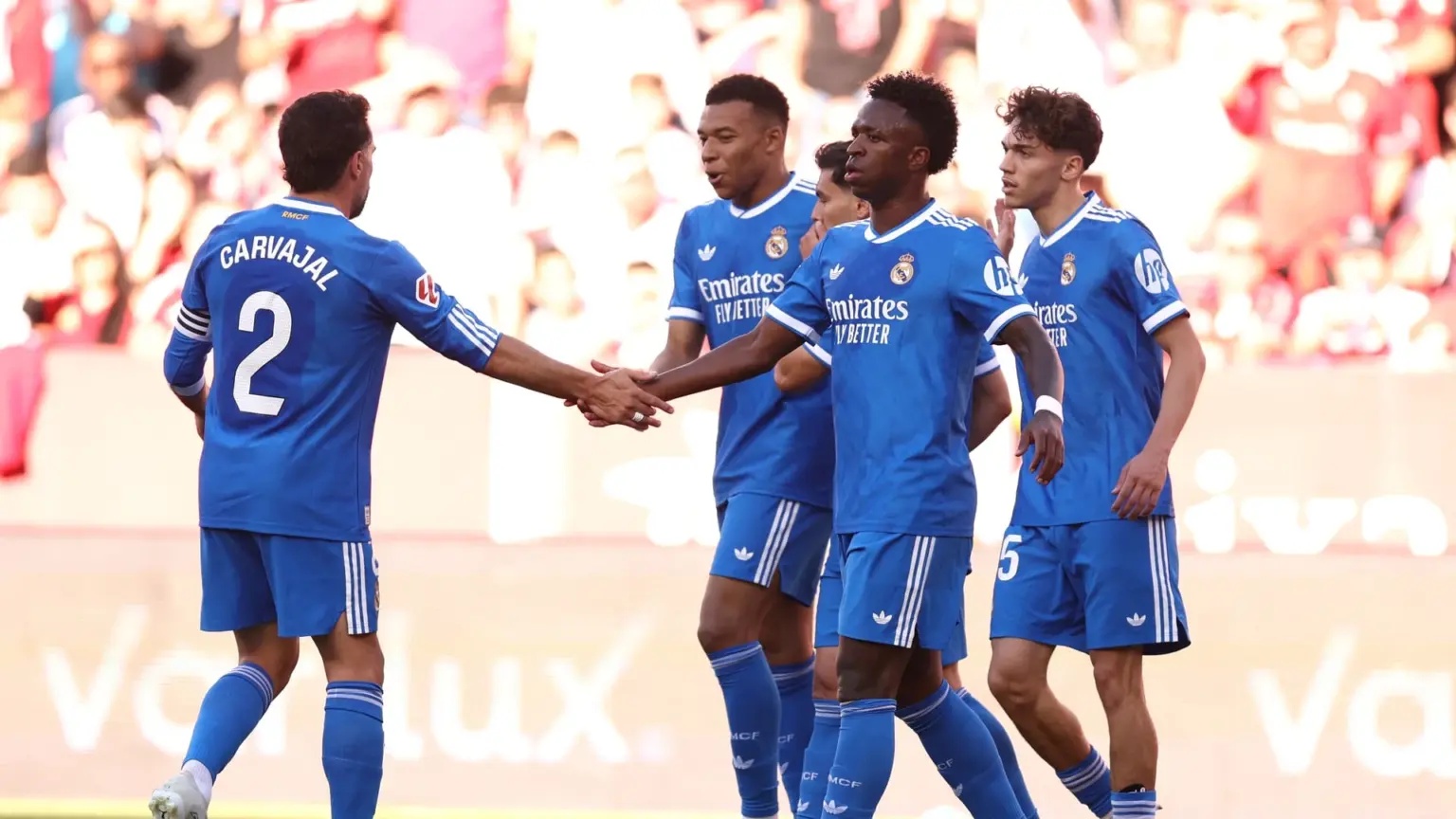 Vinícius Júnior and other Real Madrid players in blue kits on a football pitch.