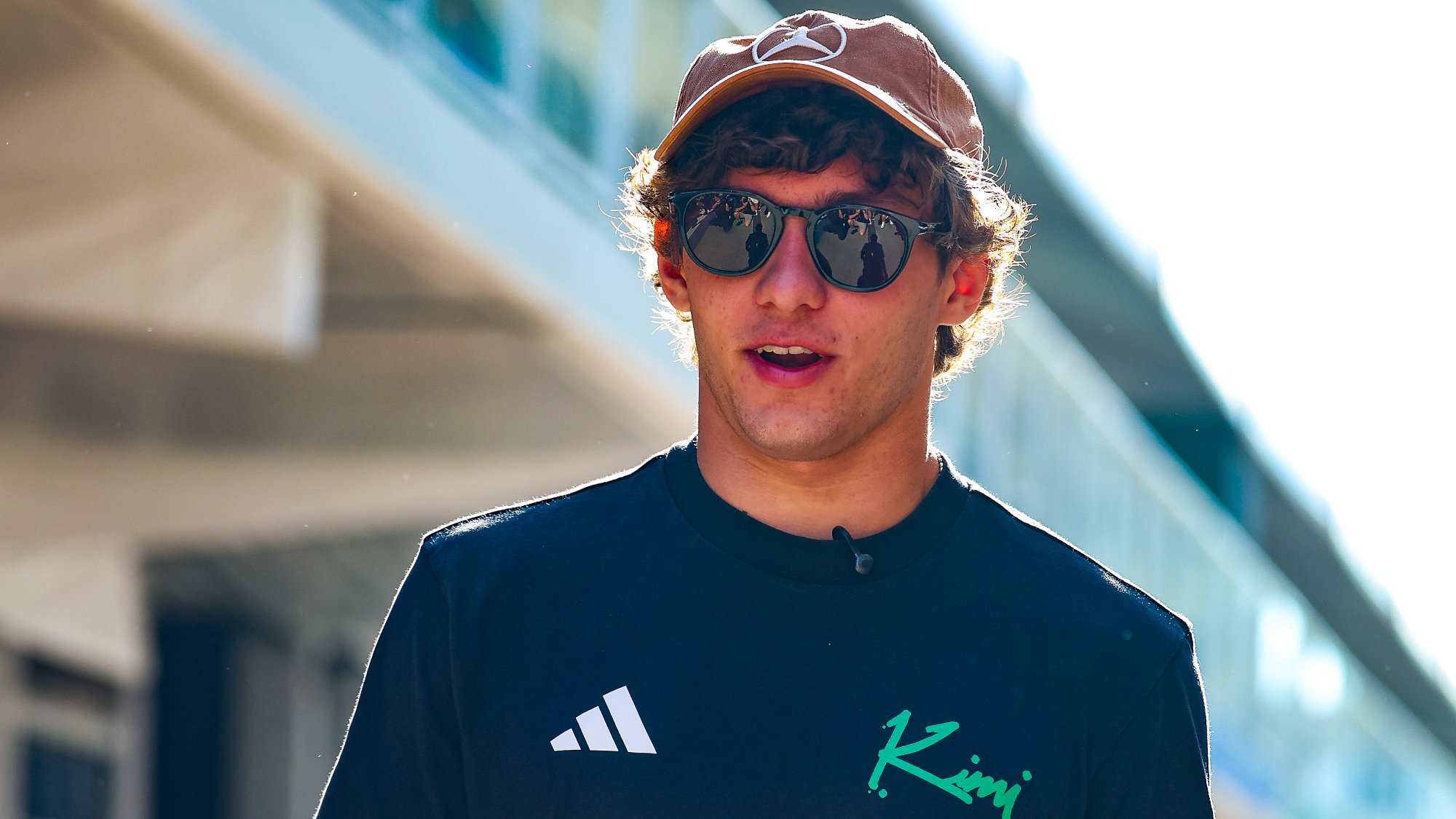F1 driver Andrea Kimi Antonelli looking onwards, wearing a cap and sunglasses.