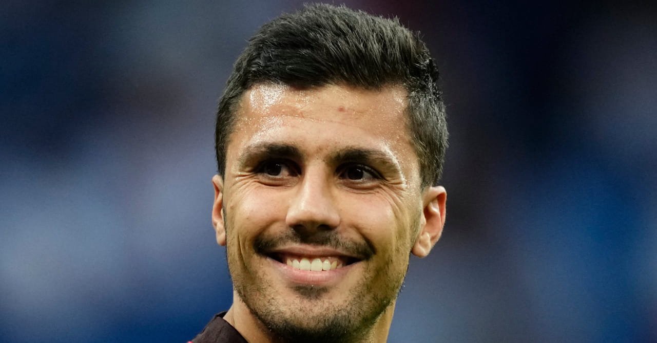 Spain footballer Rodri looking to his right and smiling in a football stadium