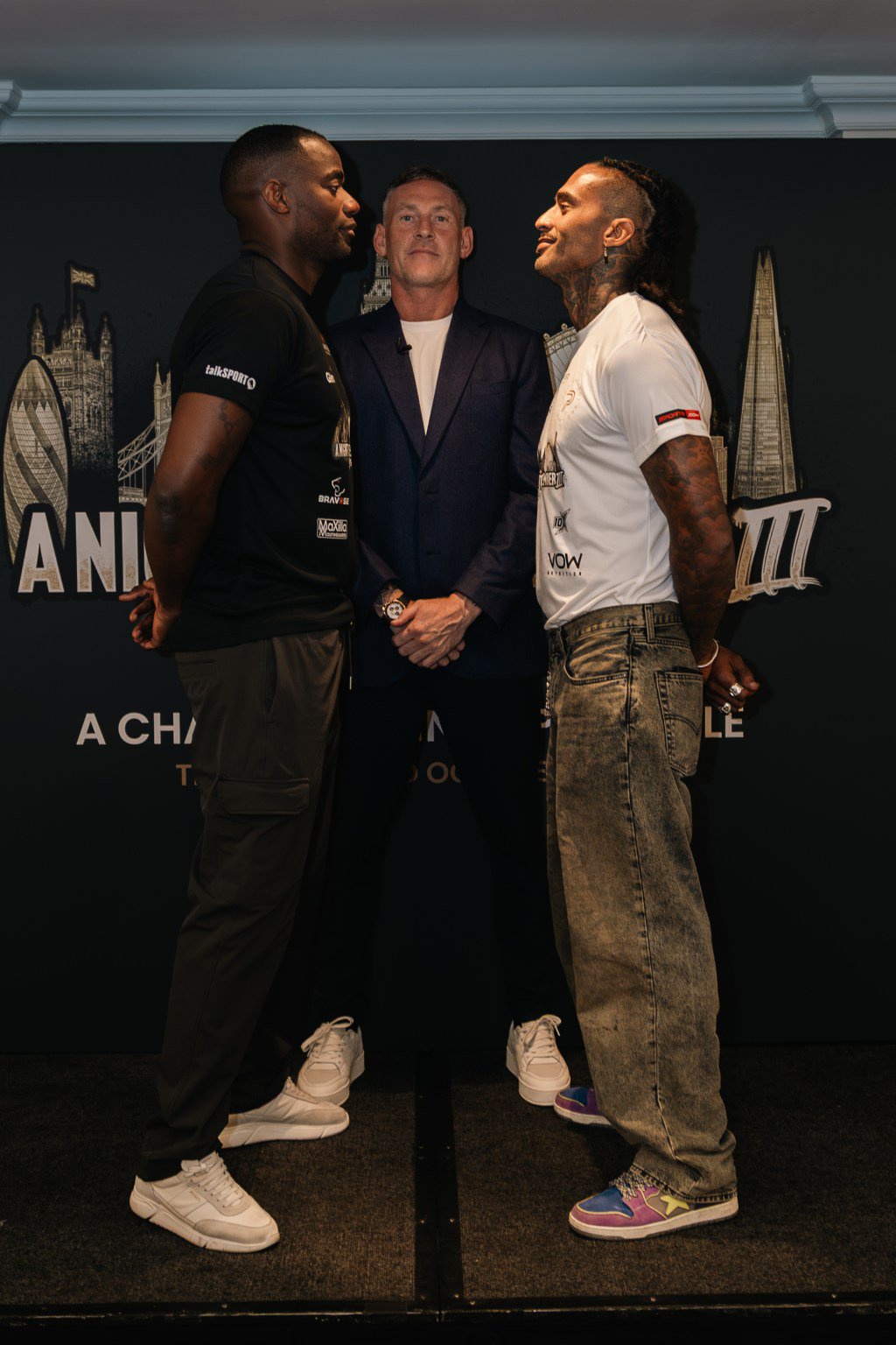 Two athletes stand face-to-face in a staredown with a man standing between them.