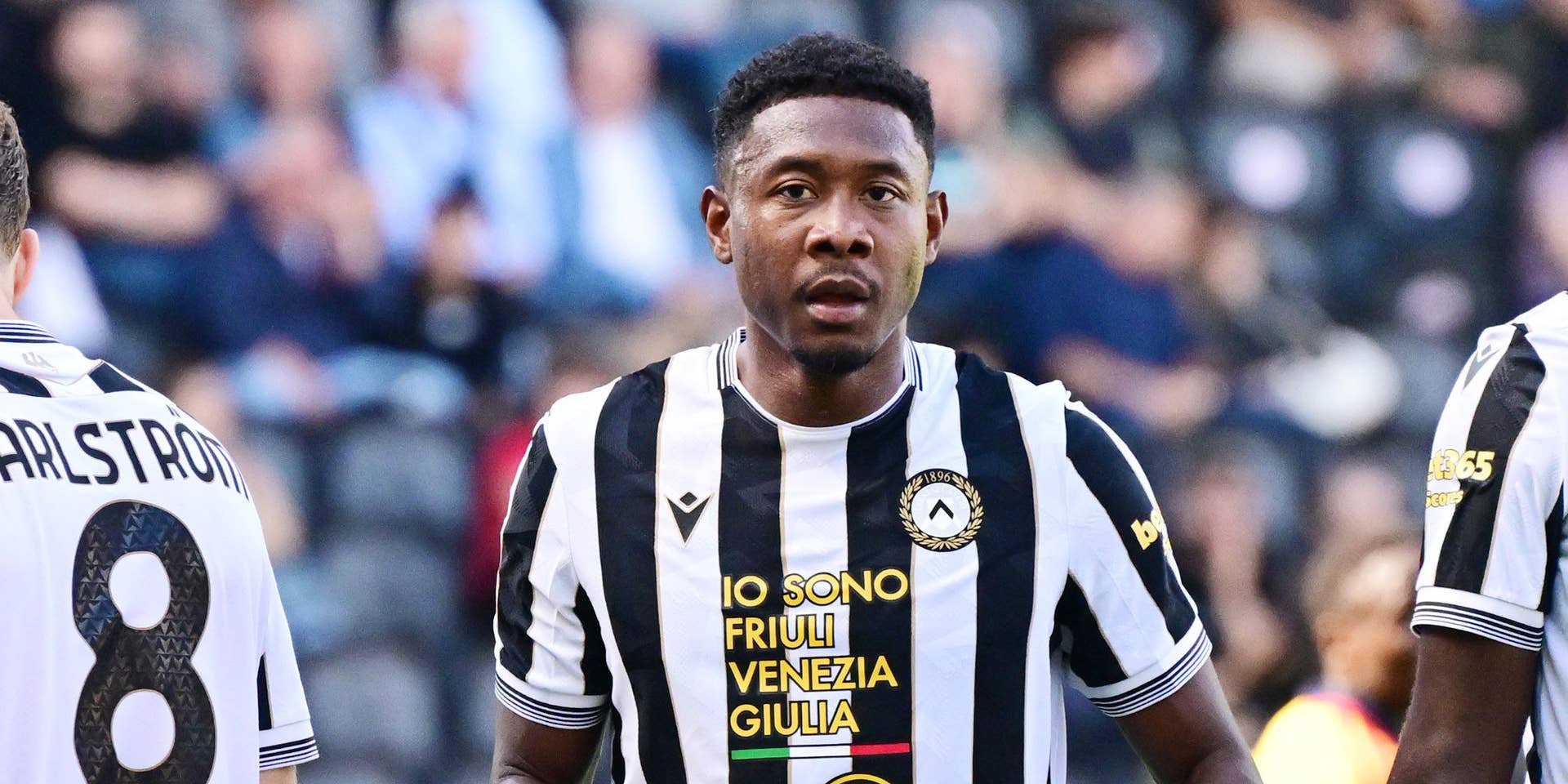 David Alaba blickt im schwarz-weiß gestreiften Trikot von Udinese Calcio konzentriert auf das Spielfeld.