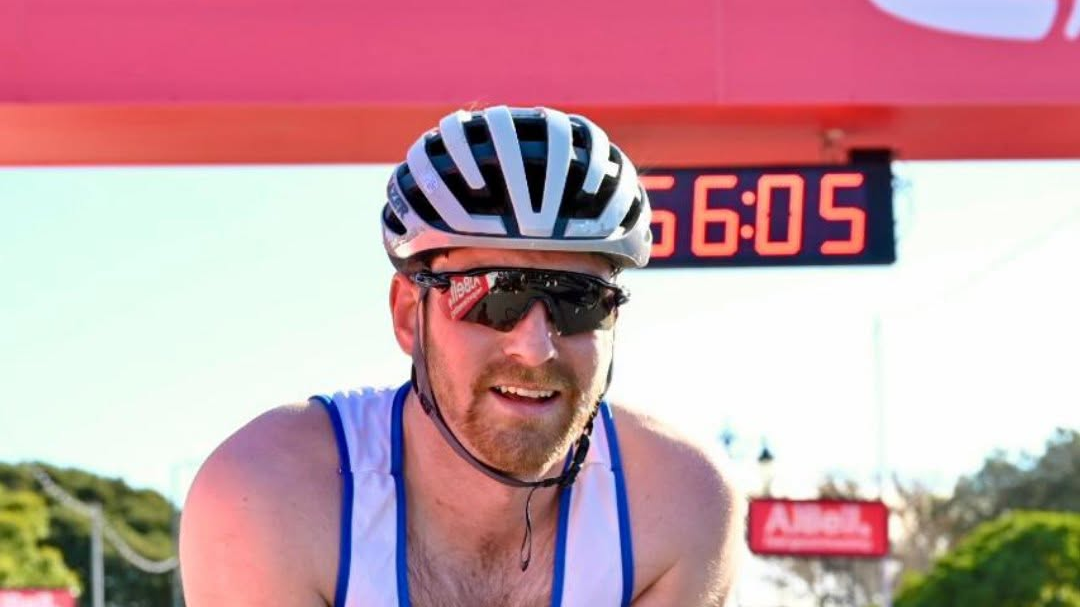 Dale Muffett, wearing a white crash helmet and a white and blue vest, smiling after the race on a pleasant day.