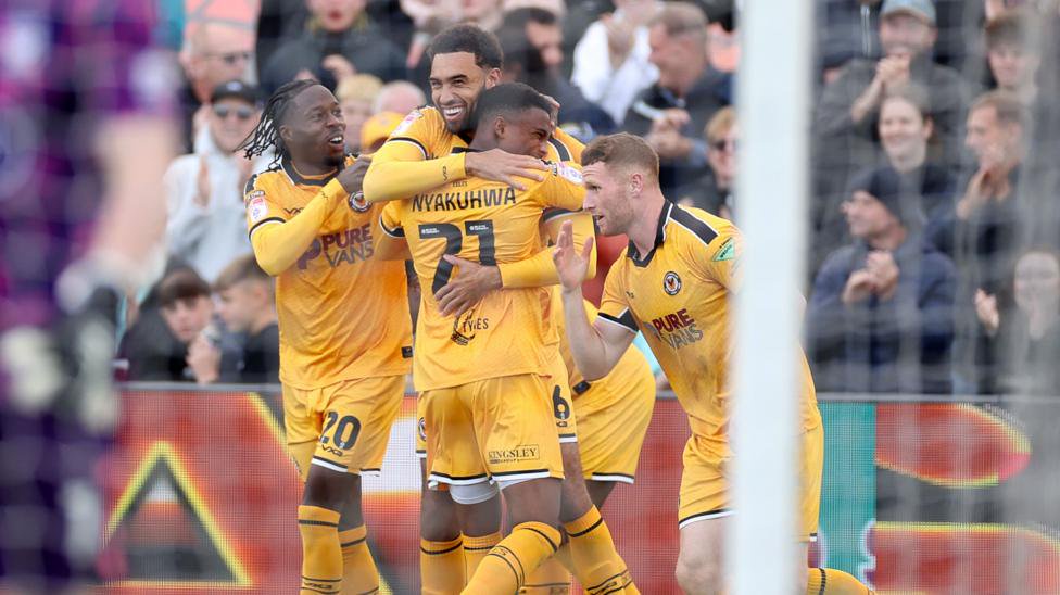 Kion Etete celebrates with Newport team-mates in all amber kit