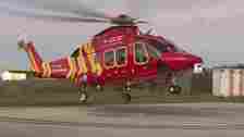BBC Cornwall Air Ambulance seen taking off, with mainly red and some yellow in its design