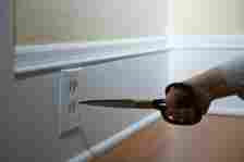 A small child's hand is holding a pair of scissors very close to an electrical outlet, posing a dangerous situation