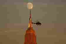 A Blade helicopter flies past the Empire State Building as a 95 percent illuminated waxing gibbous moon rises at sunset in New York City on October 26, 2023, as seen from Hoboken, New Jersey.