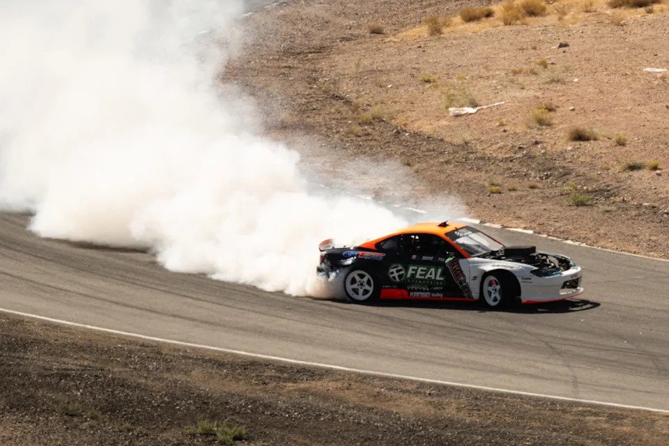 A drifting car emitting tire smoke on a winding track.