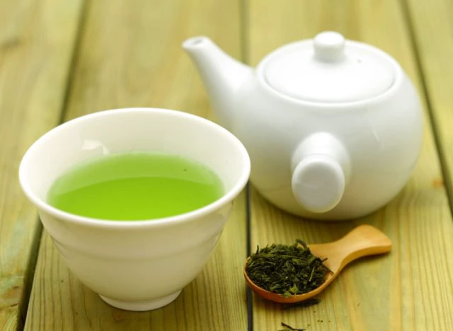 green tea in cup and teapot and tea leaves on wooden spoon