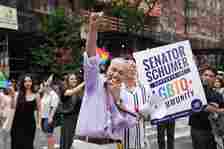 Sen. Schuck Schumer wearing a lavender shirt and raising his fist while holding a megaphone.