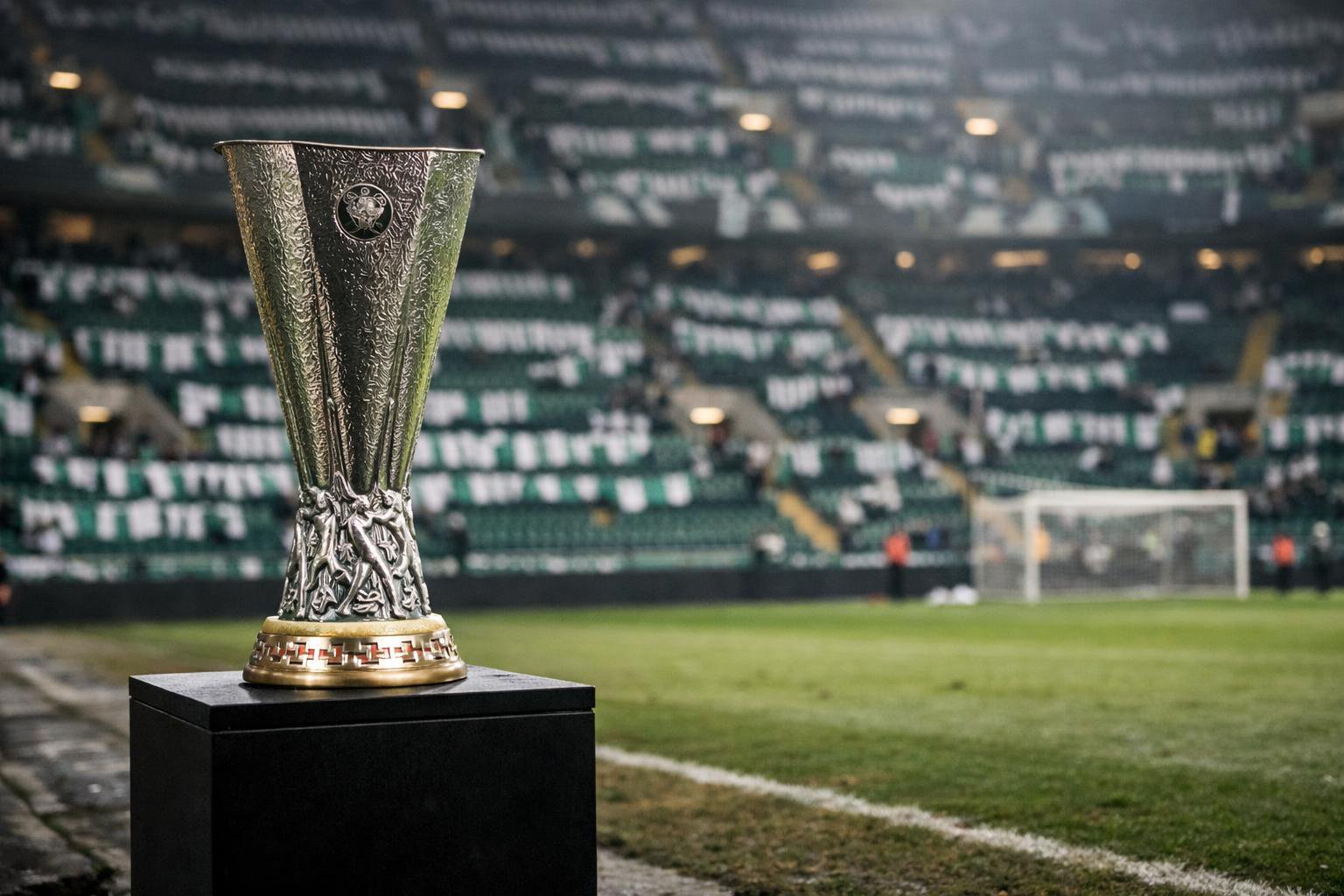 Give me the Europa League trophy sitting on a plinth at the side of the pitch with green and white scarves in the stands