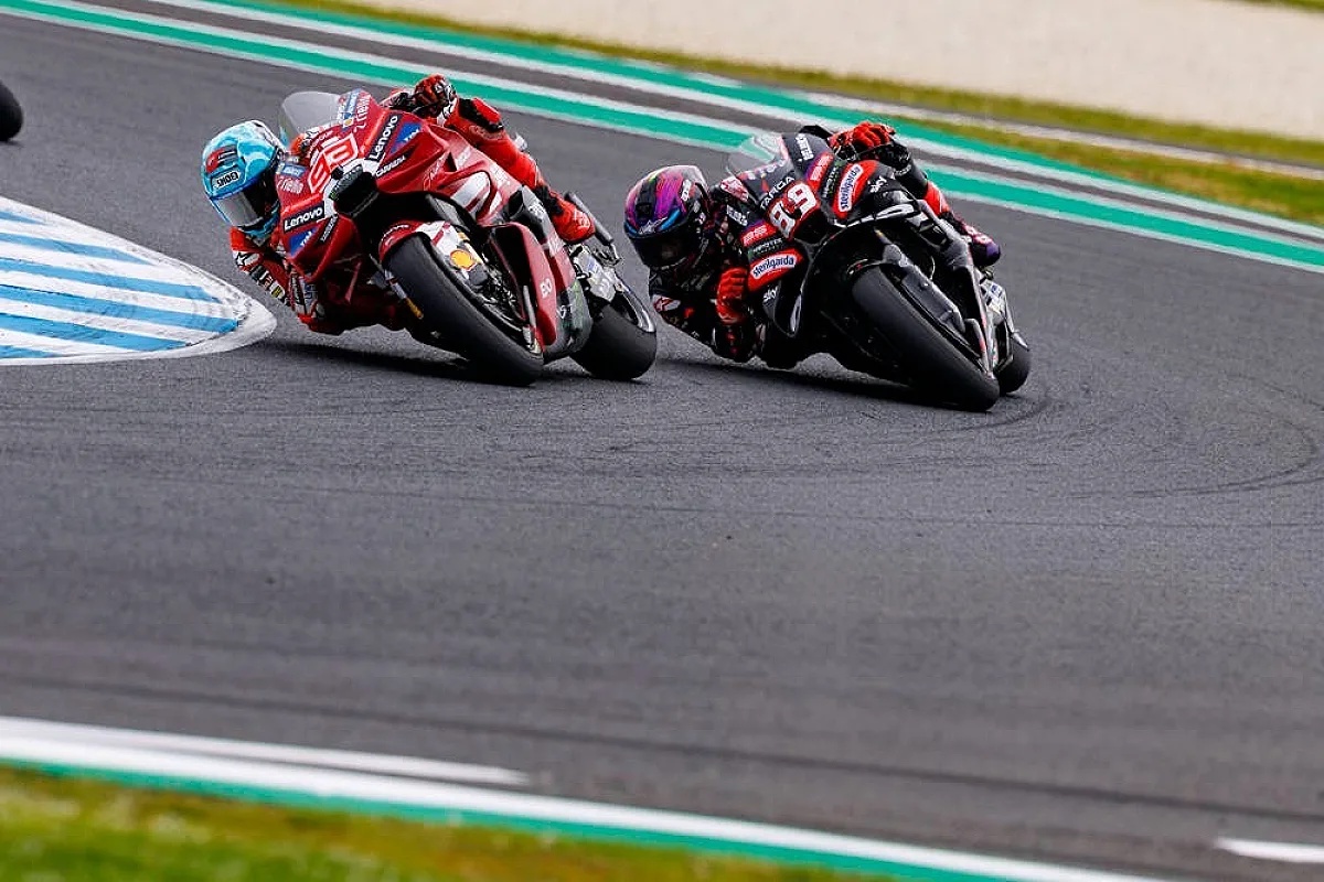 Two MotoGP riders race side by side on red and black Ducati bikes at Phillip Island, one in a light blue helmet.