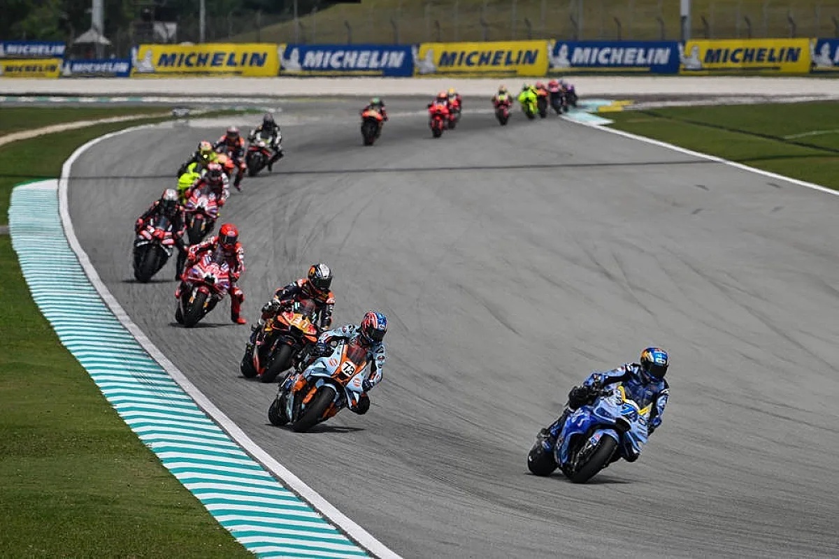 MotoGP riders race on track at Sepang, with a rider in blue leading the pack and a number 22 bike ahead, Michelin signage behind.