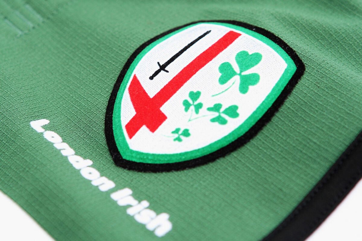 Close-up of the London Irish rugby club logo on a green jersey, featuring a sword, red cross, and shamrocks.