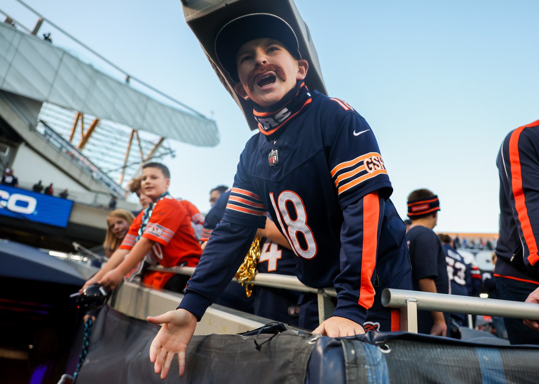 Jacob Blazyk, 13, wears a Mike Ditka mustache and cheese grater hat as he yells toward players while they warm up on the field before the Bears host the Patriots at Soldier Field on Oct. 22, 2026. (Armando L. Sanchez/Chicago Tribune)