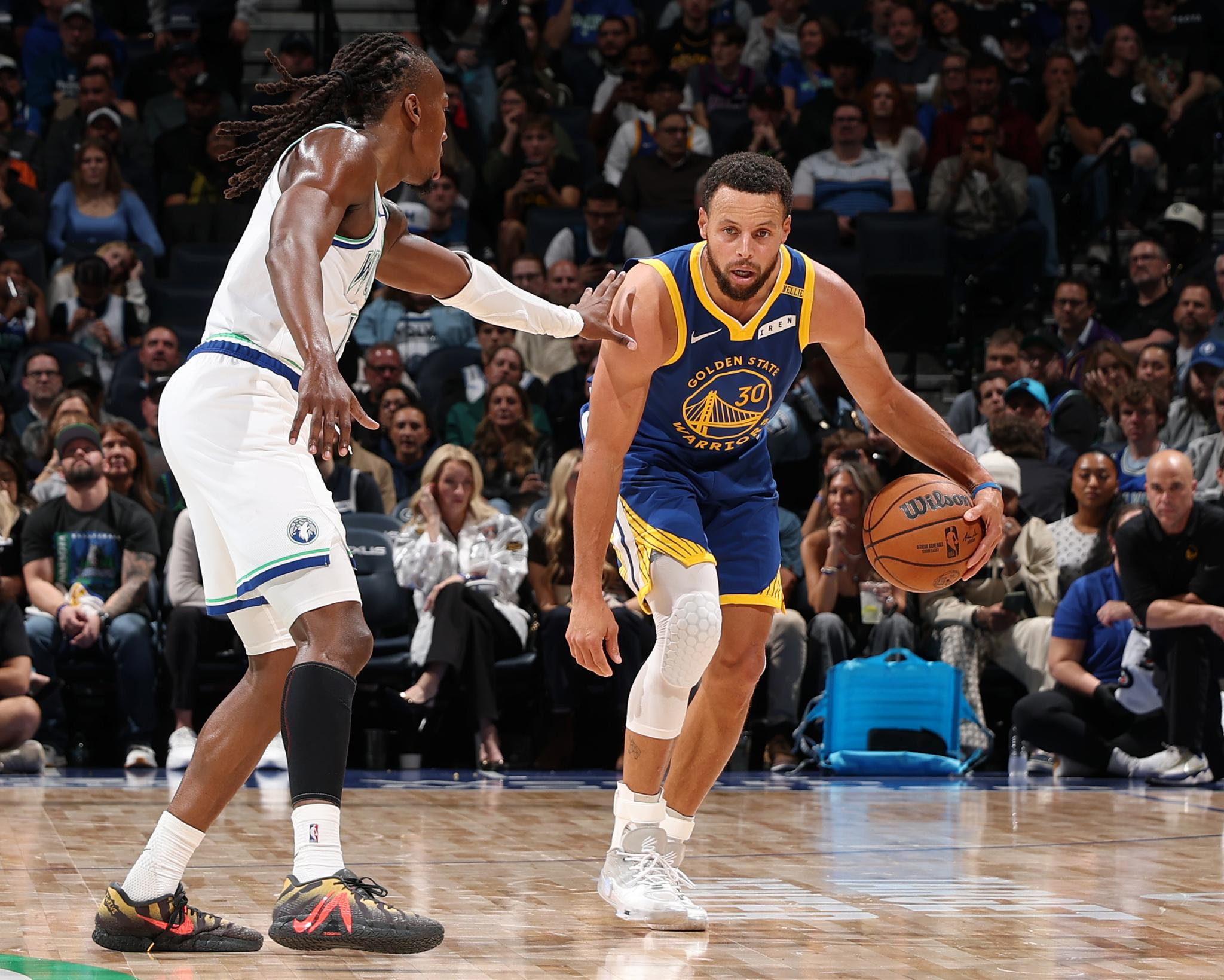 Stephen Curry of the Golden State Warriors dribbles the basketball while guarded by a Minnesota Timberwolves player.