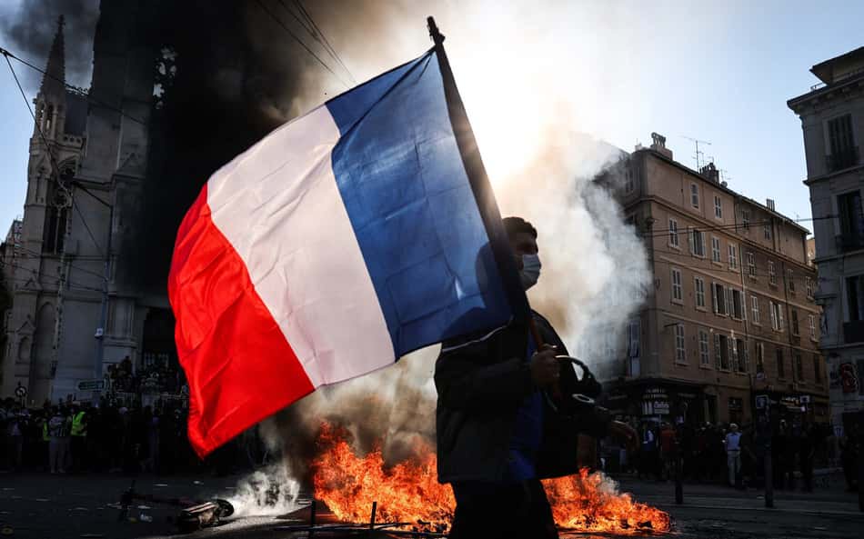 Manifestante caminha com uma bandeira da França diante de um foco de incêndio durante confrontos antes de uma manifestação contra o alto custo de vida em Marselha, no sul da França, em 17 de outubro de 2026.