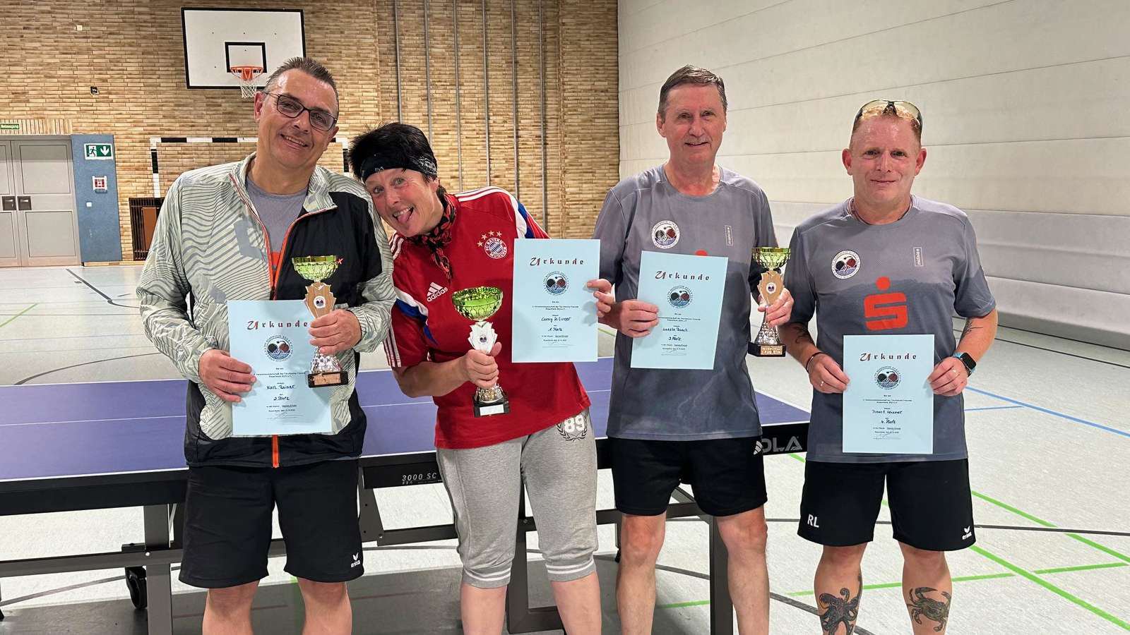 Die Sieger der Tischtennis-Vereinsmeisterschaft der TTF Rosenheim: Rainer Karl, Siegerin Conny Kifinger, Laszlo Rauch und Robert Leissner mit Urkunden und Pokalen an einer Tischtennisplatte.