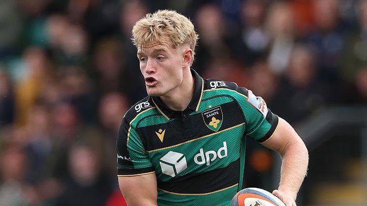 Fin Smith, in action for Northampton Saints, looking up with the ball in his hands.
