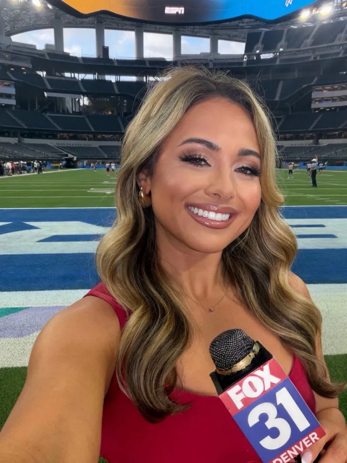 A woman holding a Fox 31 Denver microphone while standing on a football field.