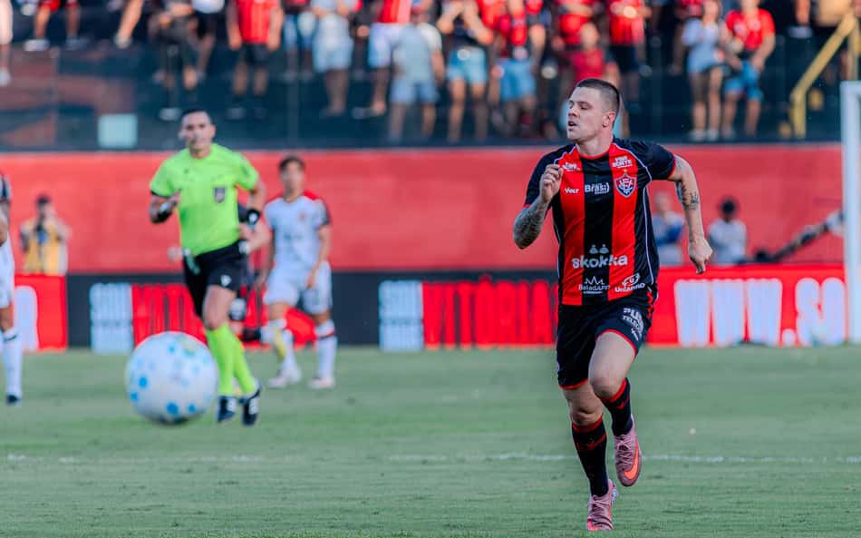 Jogador do Athletico Paranaense em uniforme rubro-negro corre com a bola durante o Brasileirão, com torcida ao fundo.