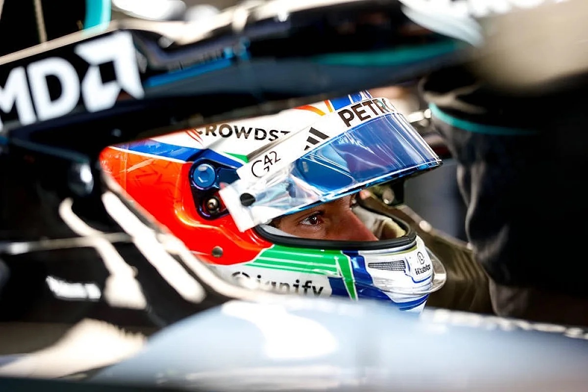 A Mercedes Formula 1 driver in a cockpit wearing a colourful helmet with a blue visor, with Mercedes-AMG Petronas livery and a Mercedes-AMG Petronas car in view
