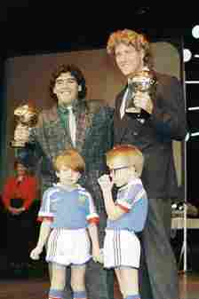 Maradona holds up his trophy alongside West German goalkeeper Harald Schumacher at the awards ceremony in Paris