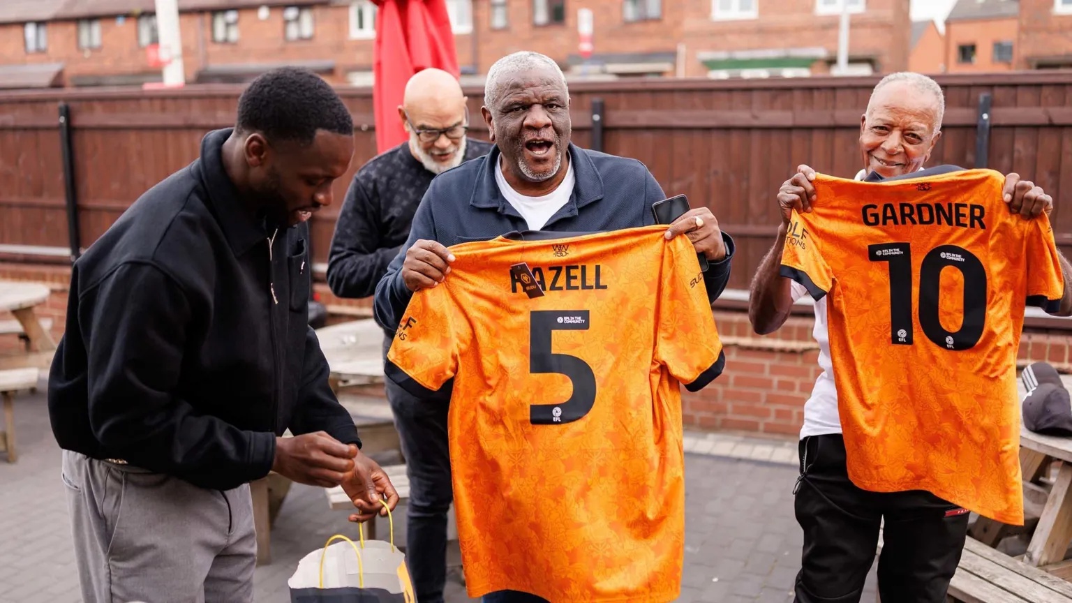 Wolverhampton Wanderers A group of men stand together, two of them are holding up gold Wolves football shirts.