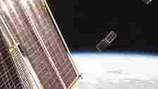 two small, rectangular satellites deploy from the international space station with earth in the background