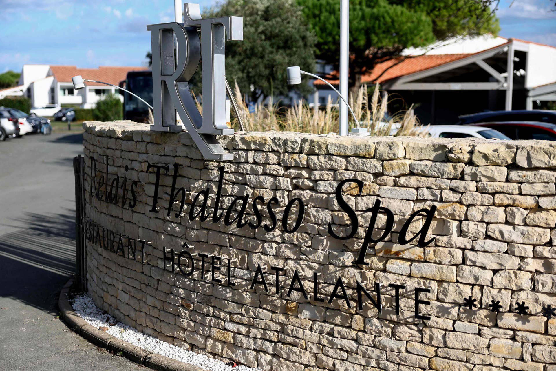 Steinmauer mit der Aufschrift "Relais Thalasso Spa RÉTA HOTEL ATALANTE" vor Hotelgebäuden.