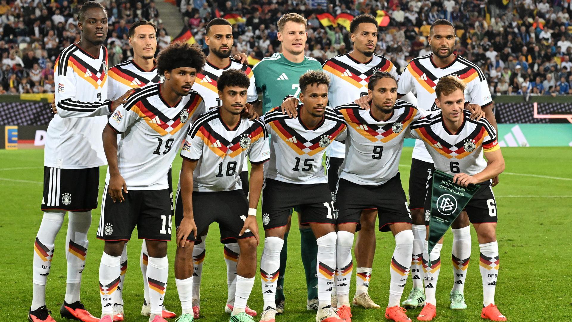 Die Spieler der deutschen Fußball-Nationalmannschaft stehen in zwei Reihen hintereinander auf dem grünen Rasen. Im Hintergrund unscharf eine vollbesetzte Zuschauertribüne. 