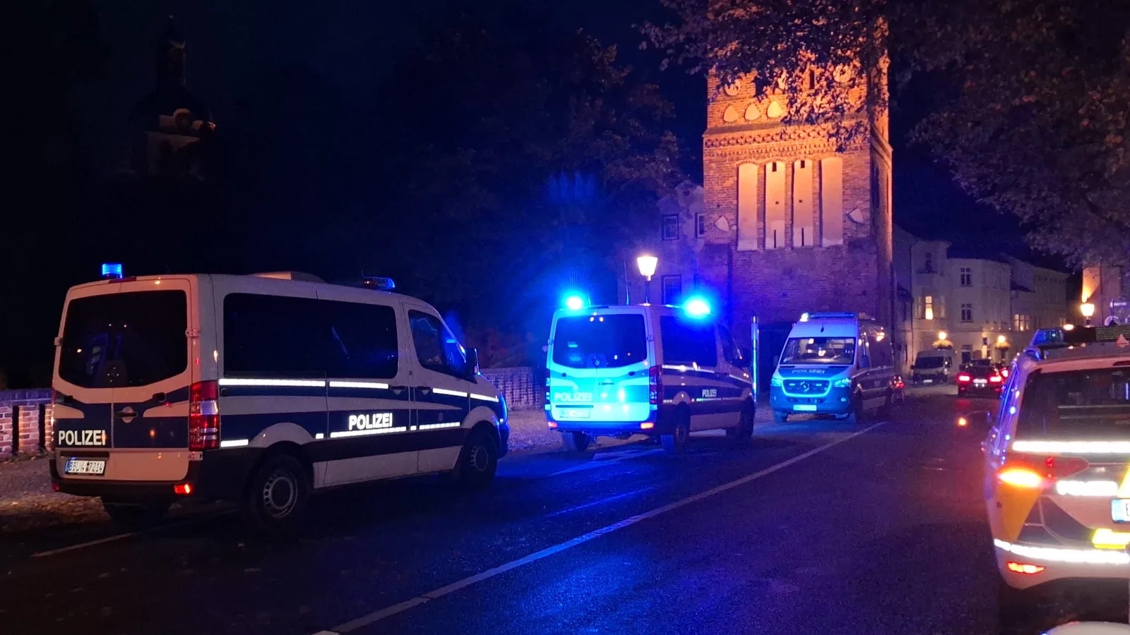 Mehrere Polizei- und Einsatzfahrzeuge mit Blaulicht stehen nachts vor einer beleuchteten Kirchturmfassade