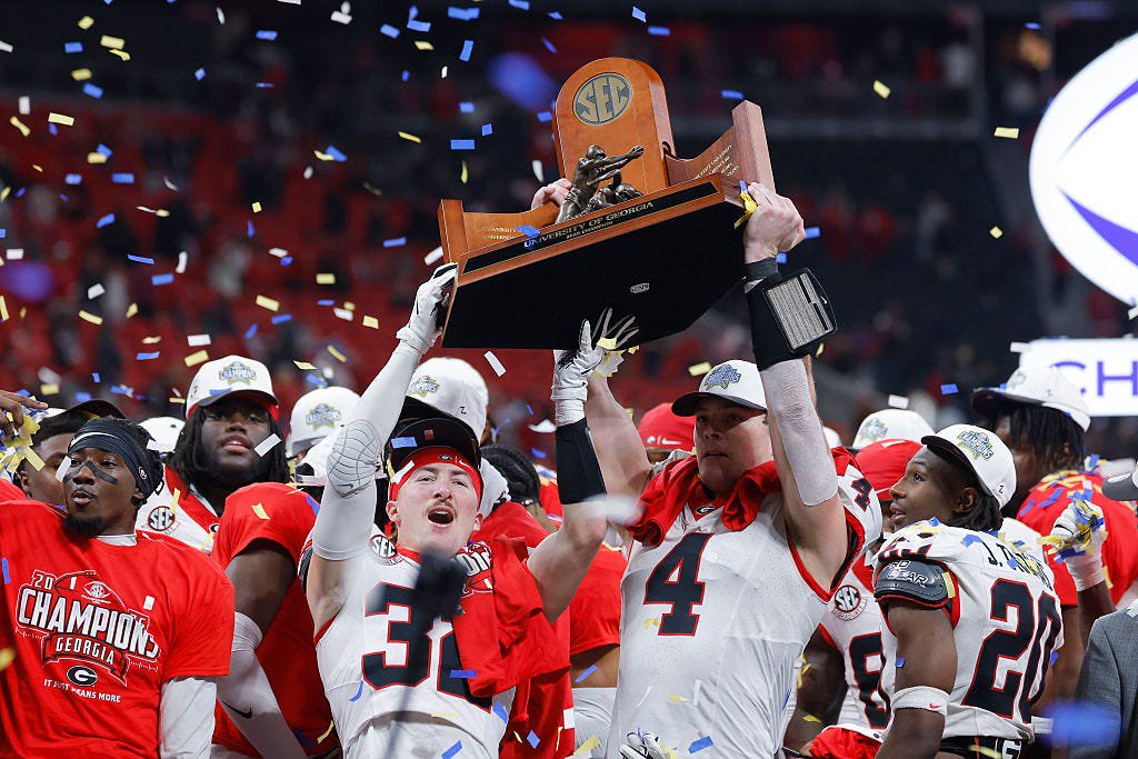 Cash Jones (32) and Oscar Delp (4) of the Georgia Bulldogs raise the 2025 SEC Championship trophy after defeating the Alabama Crimson Tide 28-7 at Mercedes-Benz Stadium on December 06, 2025 in Atlanta, Georgia. (Photo by Todd Kirkland/Getty Images)