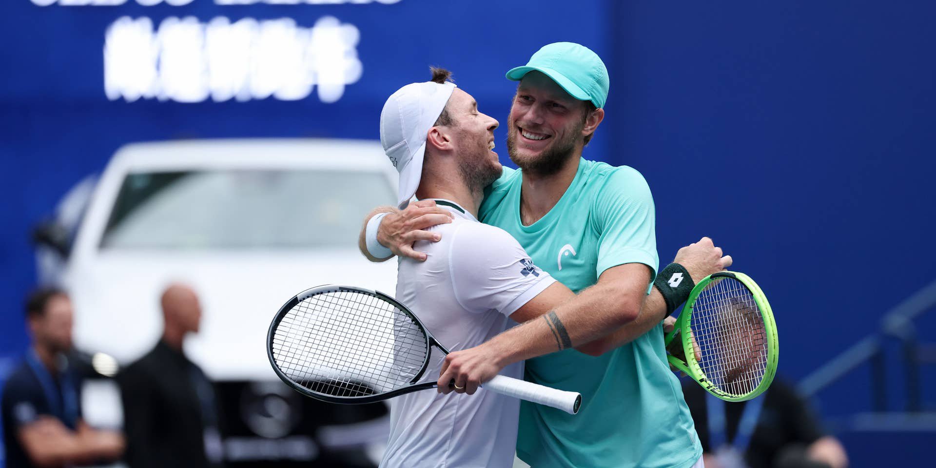 Zwei Tennisspieler umarmen sich jubelnd auf dem Platz nach einem Doppelsieg.
