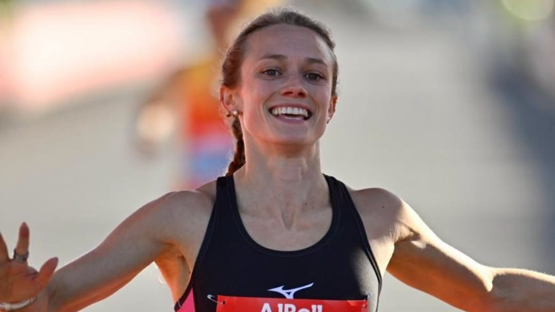 A picture of Hannah Irwin, wearing a black Mizuno running vest, celebrating as she crossed the finishing line.