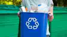 A person carries a blue recycling bin full of recyclable materials