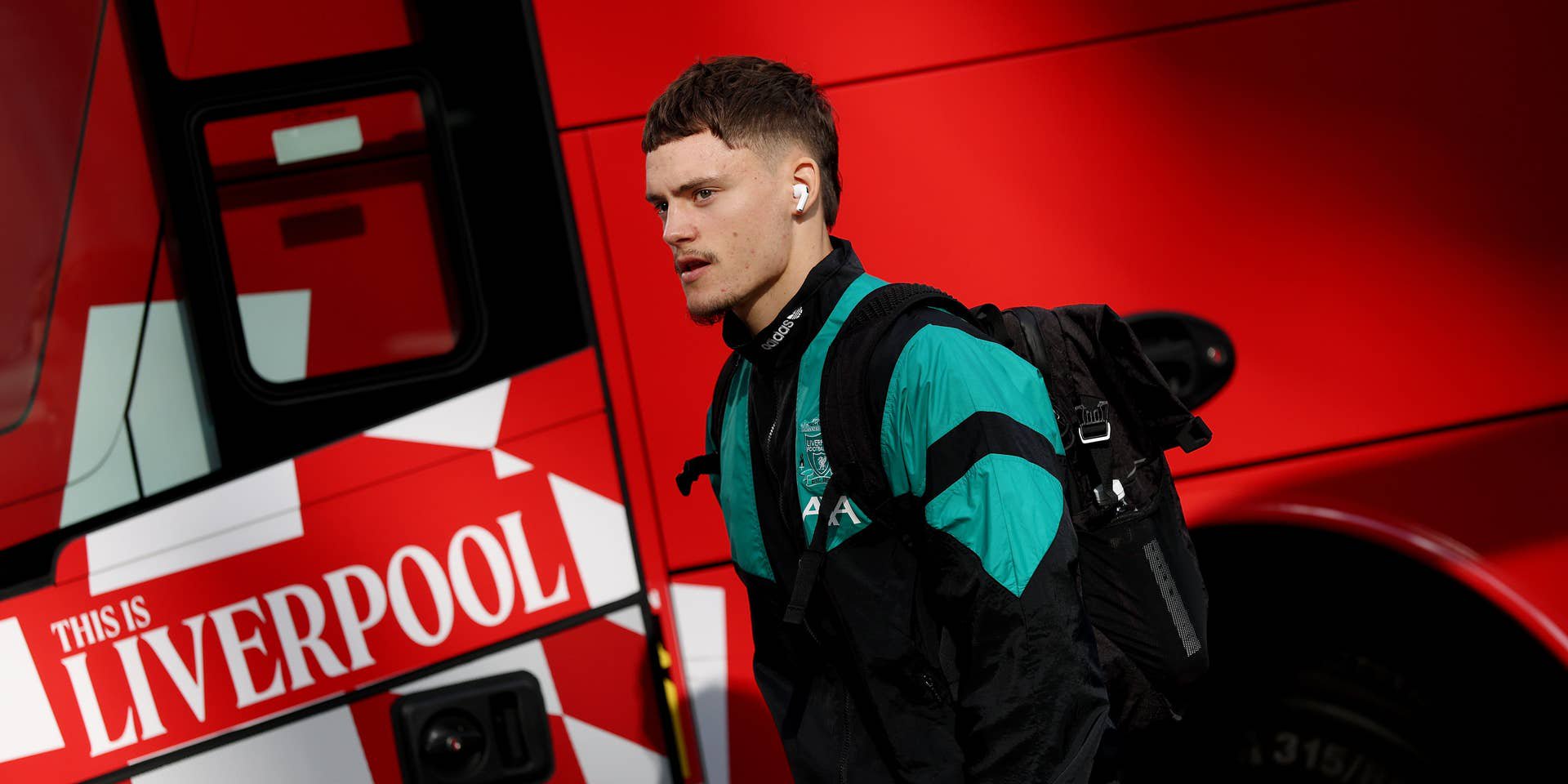 Ein junger Mann in Sportkleidung läuft mit Rucksack vor einem roten Liverpool-Bus entlang.