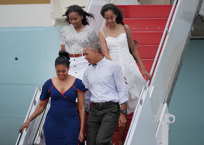 Sasha Obama shows off figure beside Malia at event, walking down stairs with parents in casual attire.