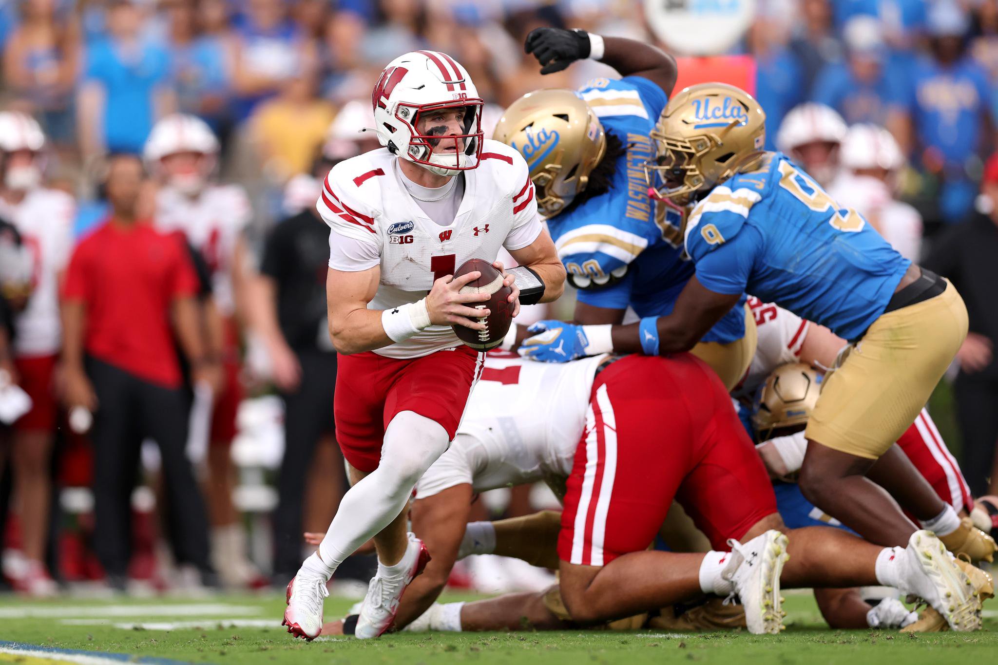 A Wisconsin football player runs with the ball while being pursued by UCLA defenders.