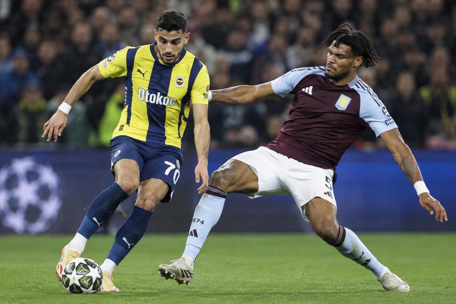 Fenerbahce's Oguz Aydin is dribbling the ball while Aston Villa's Tyrone Mings is attempting to tackle him in the UEFA Champi