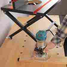 A person holding a router flanked by a router table that's foldable.