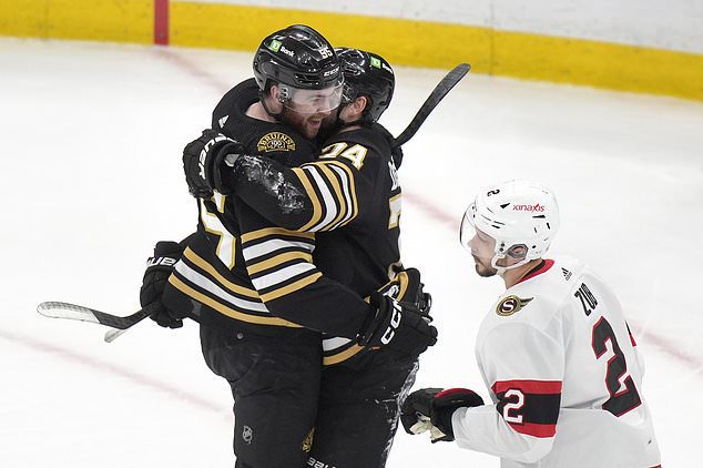 Boston Bruins right wing Justin Brazeau, left, celebrates with left wing Jake DeBrusk, center, after scoring as Ottawa Senators defenseman Artem Zub, right, skates away in the third period of an NHL hockey game, Tuesday, March 19, 2024, in Boston. (AP Photo/Steven Senne)