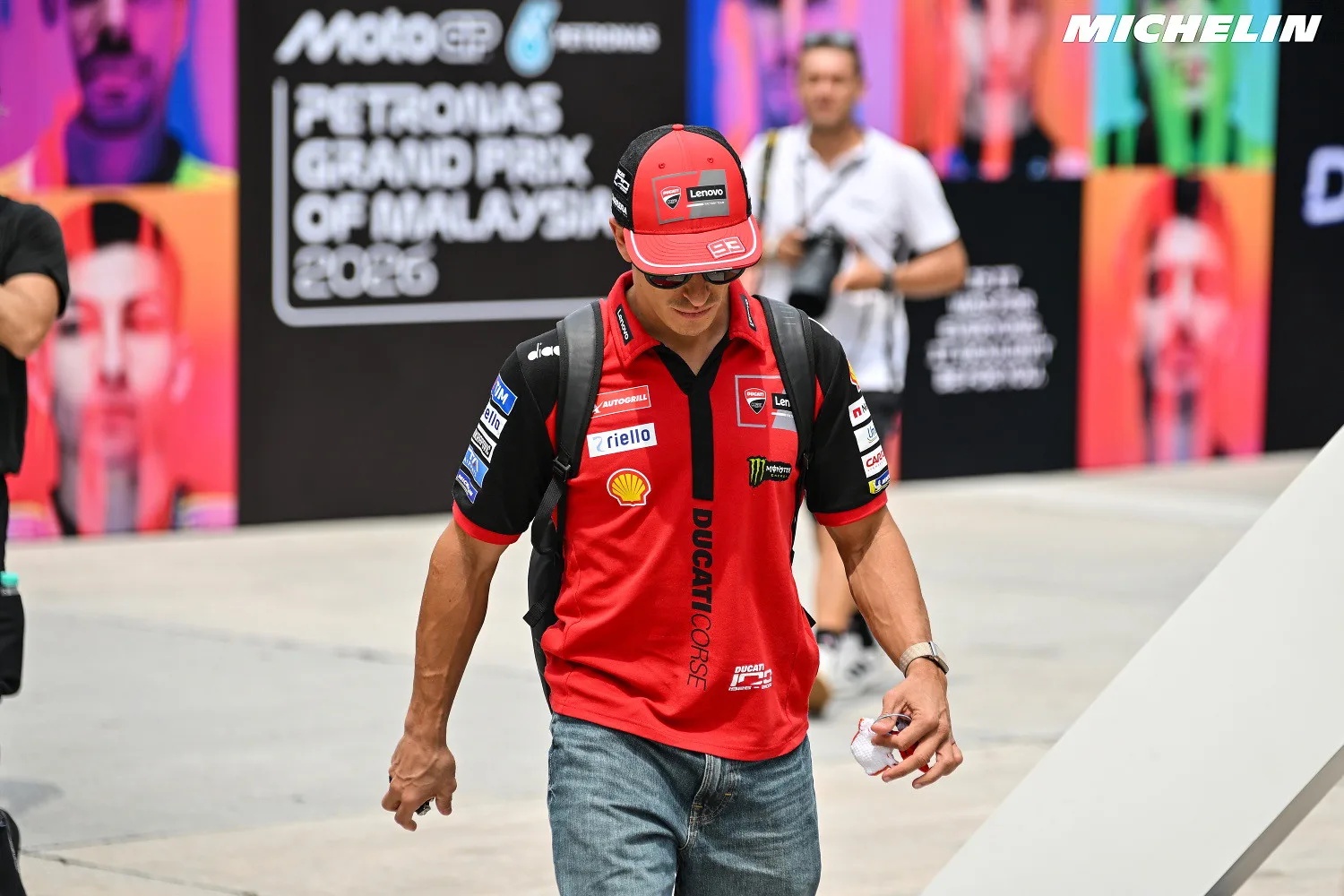 A rider in a red Ducati Corse cap and shirt walking through the MotoGP paddock at the 2026 Malaysian Grand Prix, Sepang