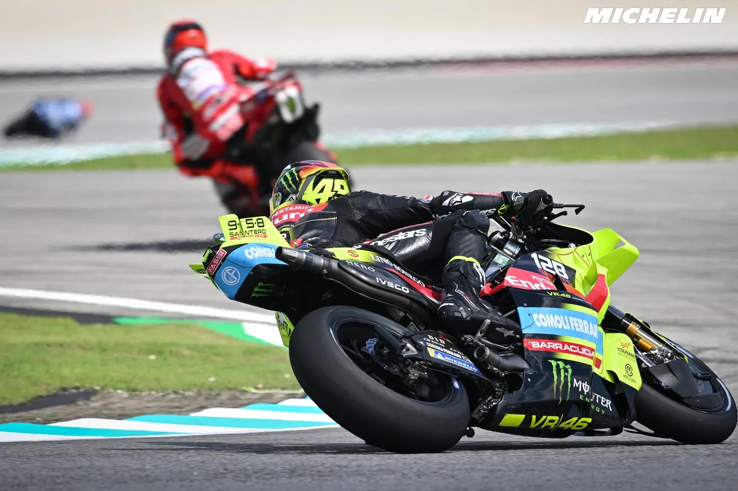 Rider leaning his Pramac-style yellow and black MotoGP bike through a corner, number 49 visible, with a red Ducati rider behind at a track Wait, I should be…